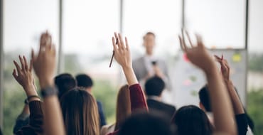 Photograph of several people from the back, with hands raised in question