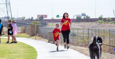 boy woman dog running on sidewalk trail at park