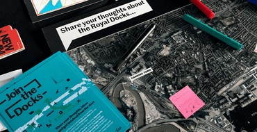 engagement materials on table, map with pens and text reading 'share your thoughts about the Royal Docks'