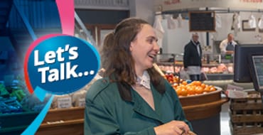 A young lady smiling and laughing in conversation with a fruit and veg grocer