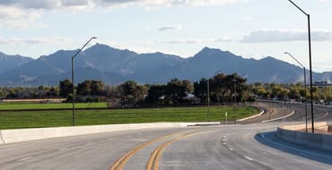 Curving roadway in Avondale with green farm fields and mountain views in the background under a partly cloudy sky.
