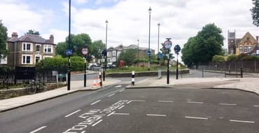 Road with width restriction beside a park approaching a residential roundabout. 