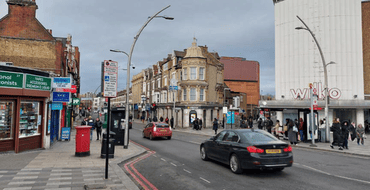 Town centre view along Cranbrook Road showing shops, active ground-floor uses, vehicles and pedestrians. Historic buildings and retail frontages create a busy high street environment and an important route connecting the station with surrounding destinations.
