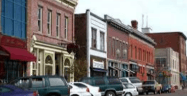 Historic downtown Laramie streetscape with multi-story commercial buildings, storefronts, and parked vehicles along the street.