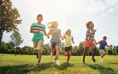 A group of children running across green grass in a park.