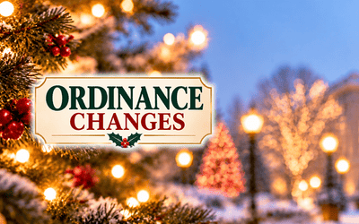 Holiday-themed banner featuring the words “Ordinance Changes” in green and red lettering, surrounded by festive Christmas ornaments, illuminated evergreen branches, holly berries, and snow, with a softly lit civic building in the background.