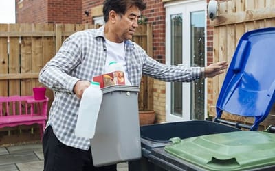A man in cargo pants and chequered shirt emptying his recycling into the outside bin