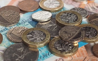 Pound coins with fifty, twenty, five and one pence coins sat on five, ten and twenty pound notes spread out.