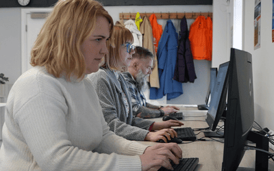 Three students in a row at a bank of desks studying on a computer, two female closest and furthest a male.