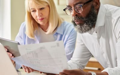 A man and woman looking at their finance paperwork with a laptop in front of them planning their finances.
