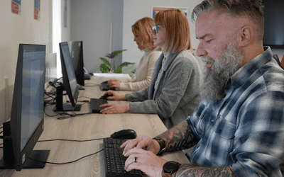 3 people sat at a desk working on individual computer