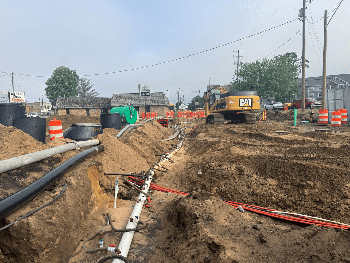Construction crews install new underground utility lines in a trench along Spring Street as part of a roadway reconstruction project.