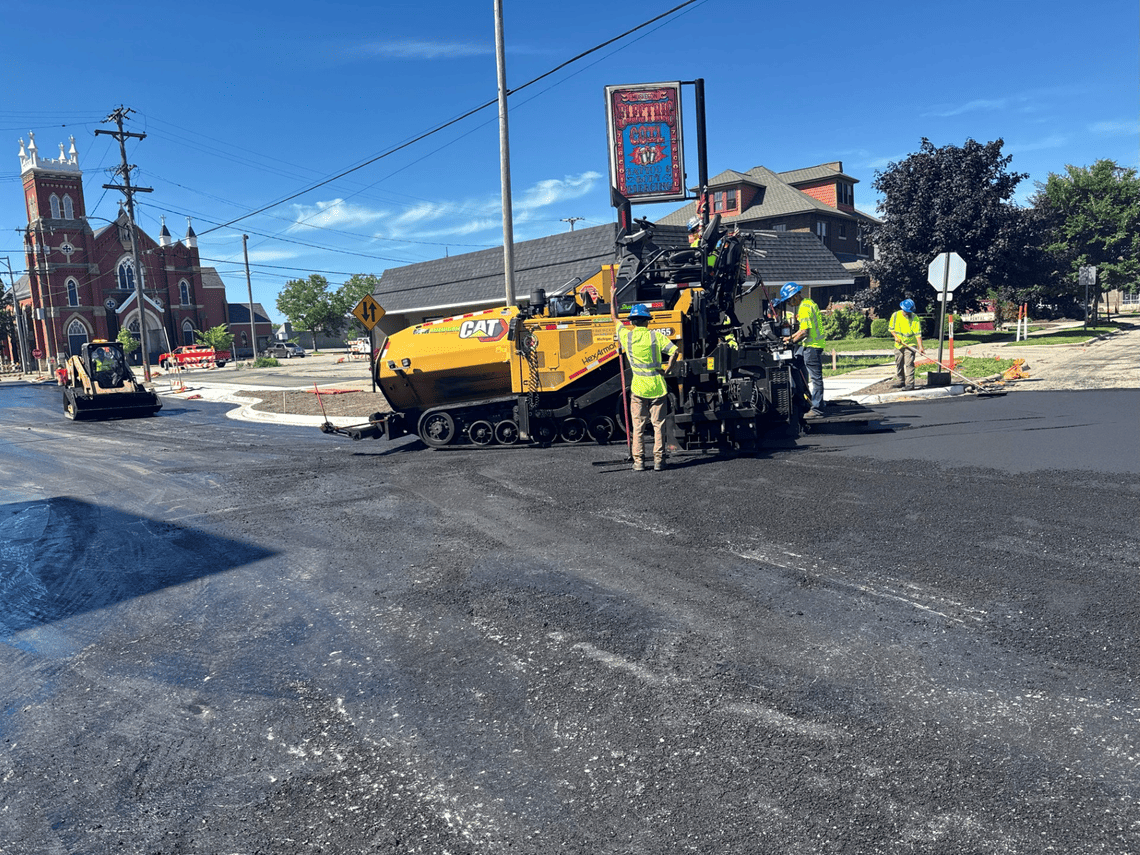 Road paving crew places new asphalt at the intersection of First Street and West Muskegon Avenue during street reconstruction.