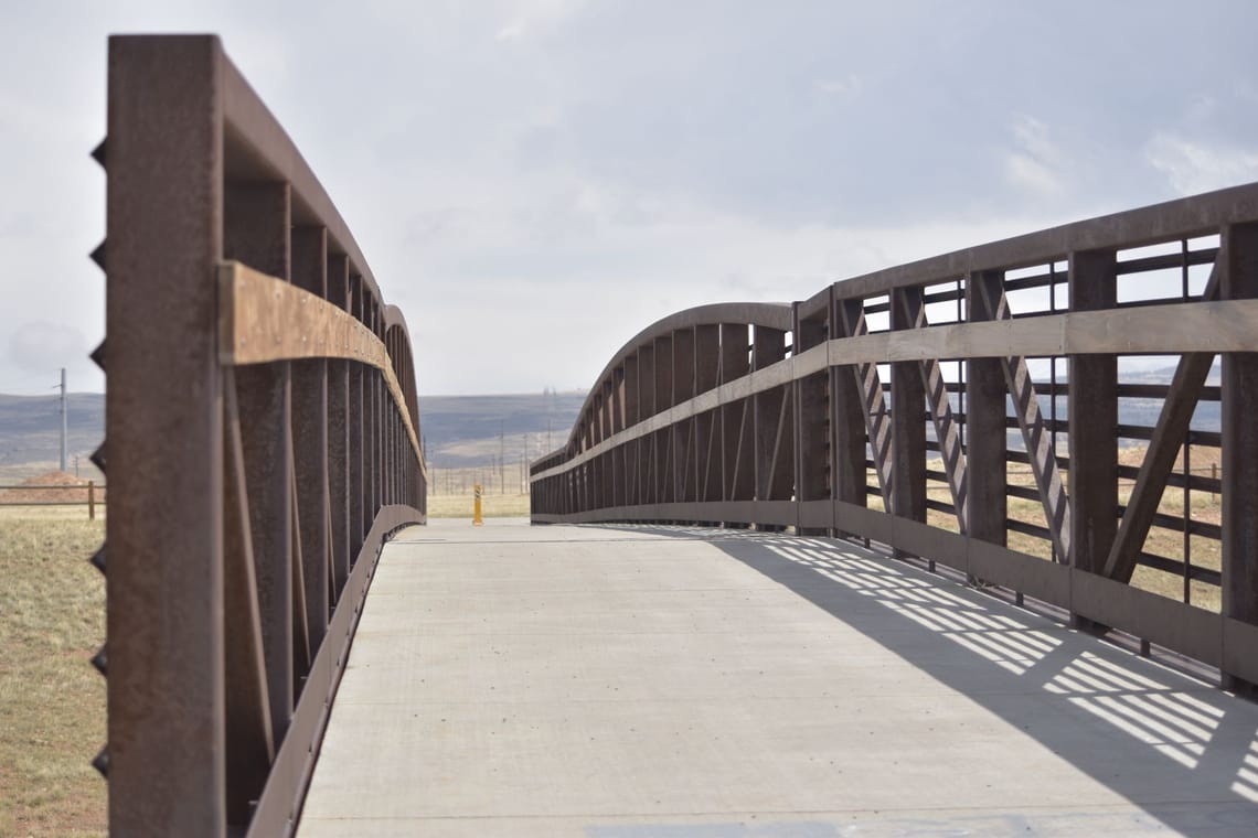 Pedestrian bridge with metal railings extending across an open landscape near Laramie, Wyoming.