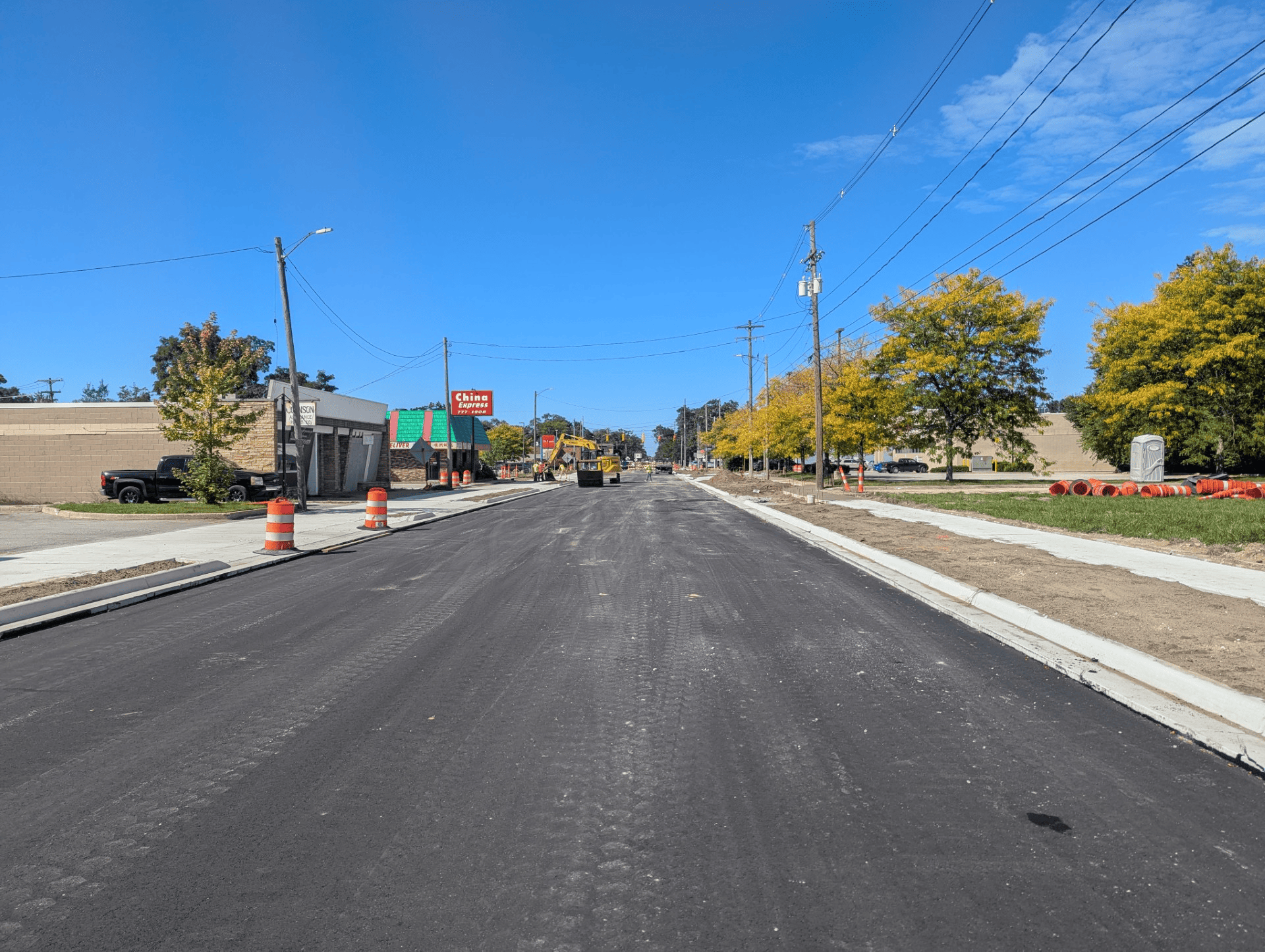 Freshly paved asphalt roadway with new concrete curbs and sidewalks, while topsoil is being placed along the roadside near Getty Street.