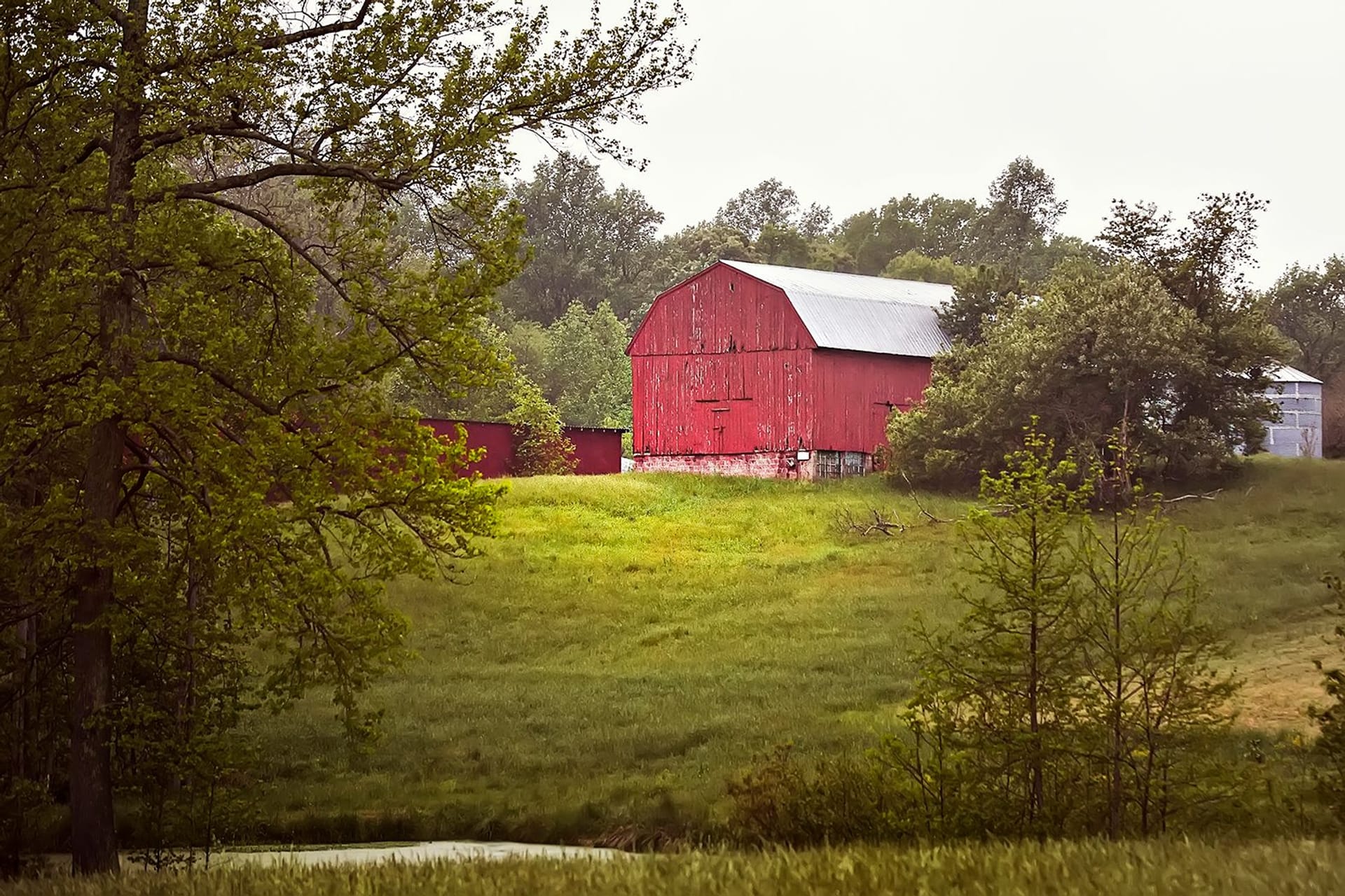 Red barn sitting on a hill overlooking a lake
