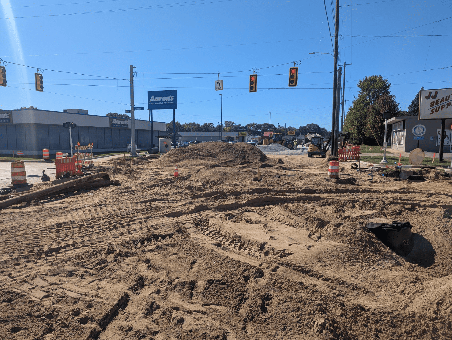 Construction at the Creston Street intersection, with new utility work, a sand base, construction equipment, and traffic signals overhead.