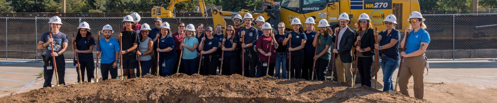 Denton Animal Services staff stand behind mound of dirt with shovels in front of excavator.
