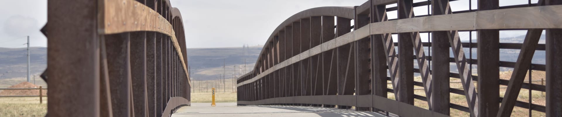 Pedestrian bridge with metal railings extending across an open landscape near Laramie, Wyoming.