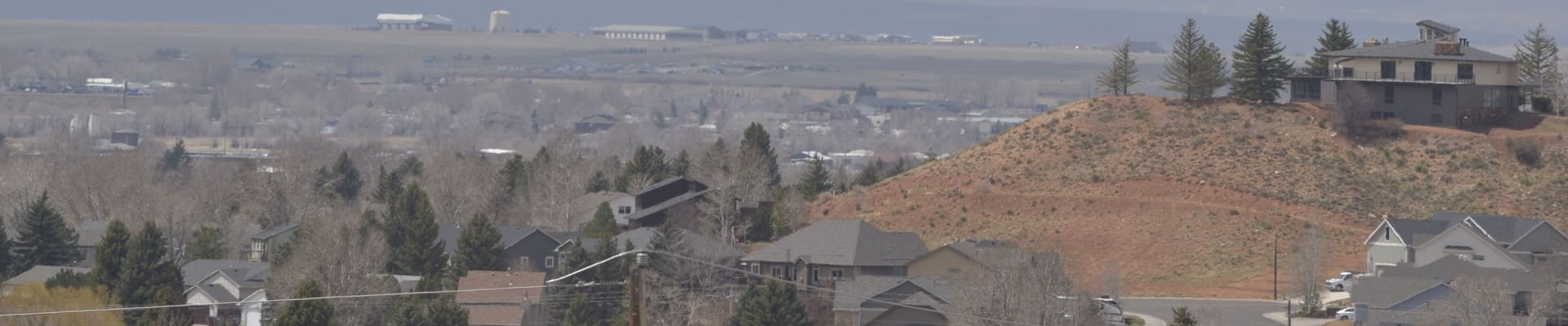 View across a Laramie residential neighborhood with homes, trees, an exposed hillside, and open landscape in the distance.