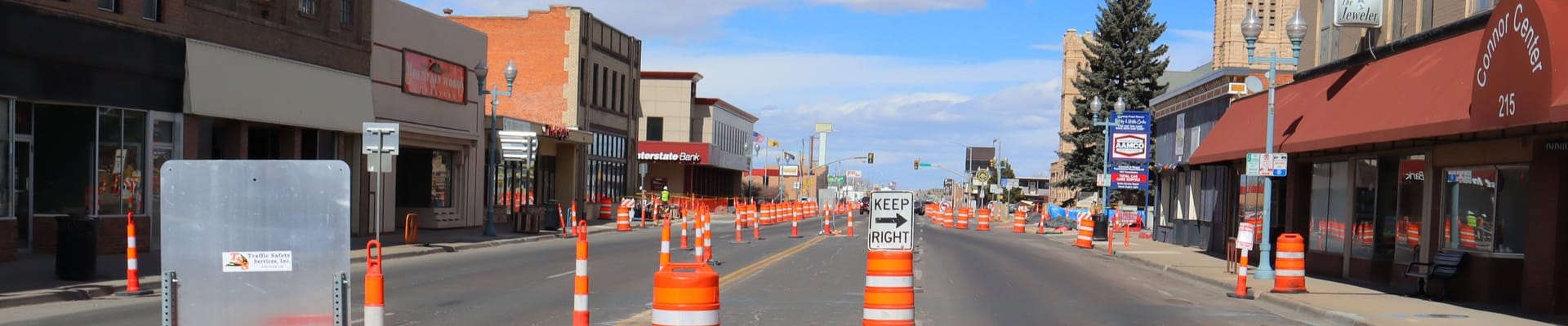 Downtown Laramie street undergoing construction, with traffic cones and barrels lining the roadway between storefronts.