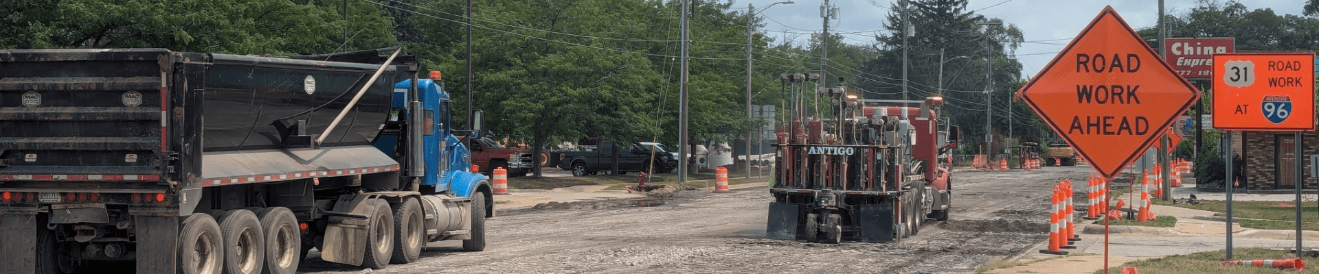Road construction crews use heavy equipment to break up and remove old concrete pavement on Getty Street. Construction barrels and road work signs line the roadway, with exposed pavement and debris visible in the foreground.