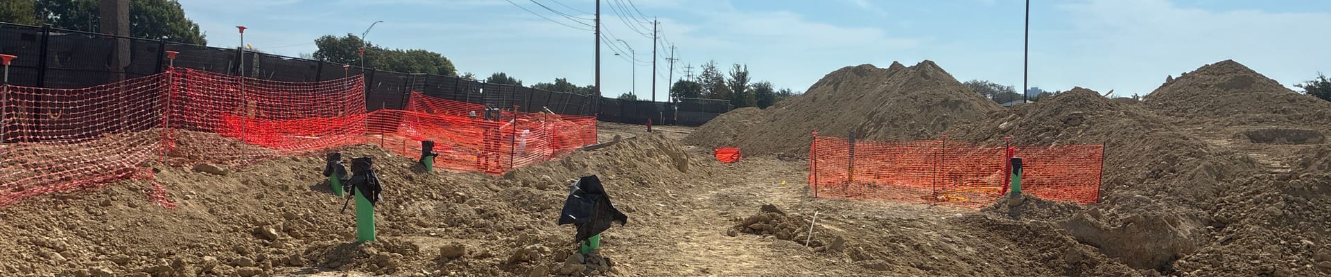 Construction site, orange fencing and green pipes protruding from ground.