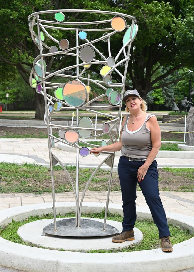 Artist standing next to an 8’ tall stainless steel sculpture with custom-laminated outdoor-grade colored, dichroic glass; the glass showcases different colors when viewed from different directions