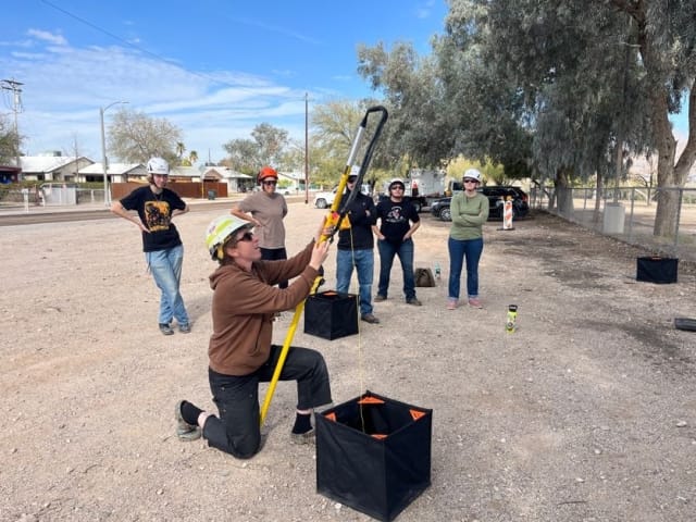 Group of students gather around an instructor who demonstrates a piece of equipment.