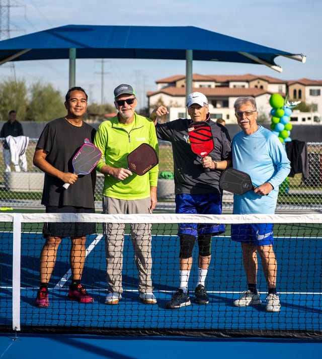 Group of 4 men standing on a pickleball court smiling while holding pickleball paddles