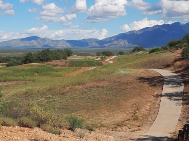 a paved path extends over a grassy hill. Mountains line the horizon. 