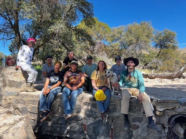 a group of students sit on a rock bed smiling at the camera. 