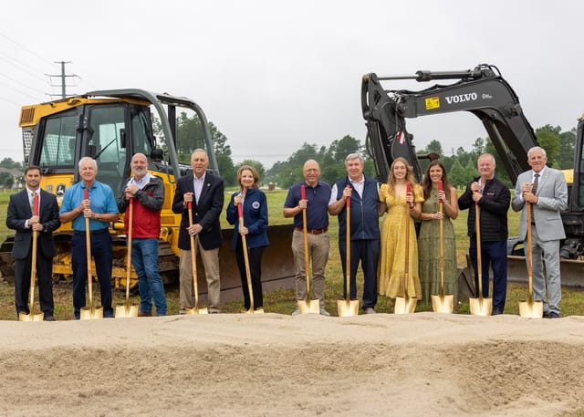 Officials holding shovels in front of heavy machinery