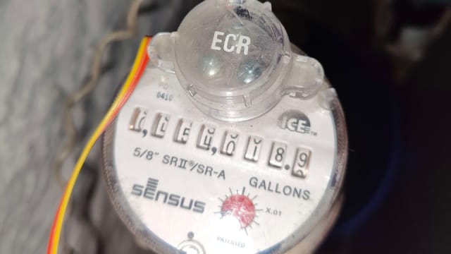 Older metal residential water meter (Sensus SR2) with a circular register and worn metallic body.