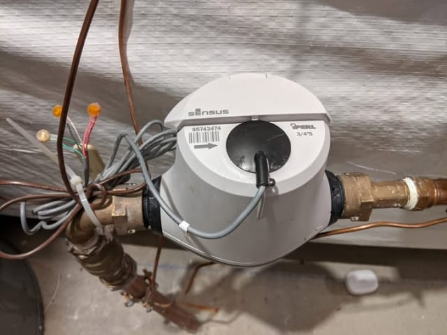 Grey plastic residential water meter (Sensus iPerl) with a digital display and rounded casing.