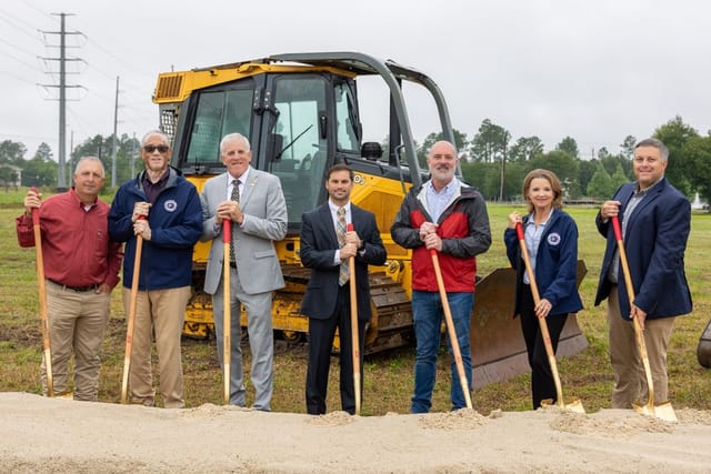 Officials holding shovels in front of heavy machinery