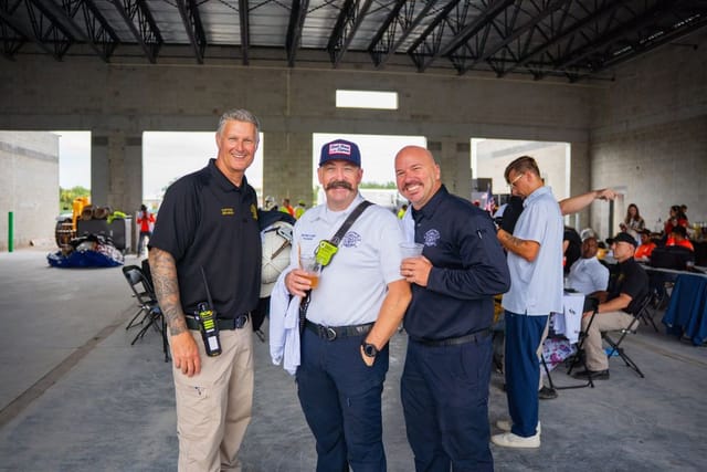 three firefighters smiling in the bay under construction at station 81