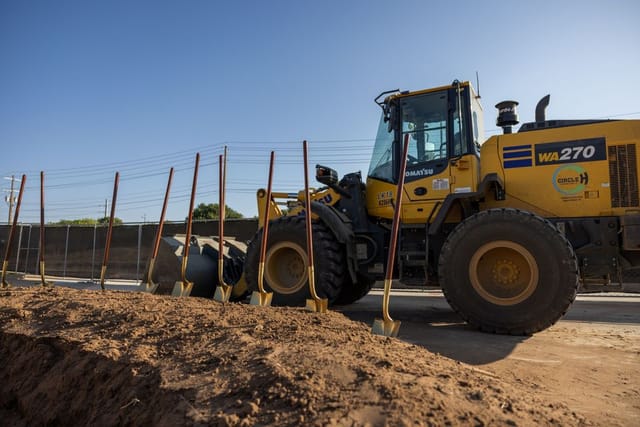 shovels standing in dirt, excavator in background