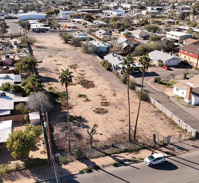 Aerial image of a barren lot nested within a neighborhood of houses. There are a few palm trees along the perimeter of the lot. 