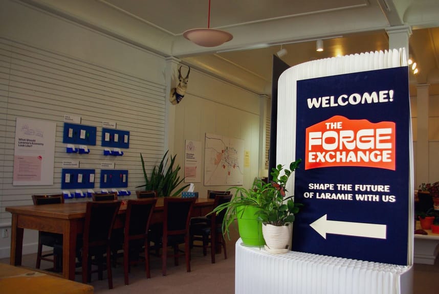Image of the indoor Forge Exchange space with tables and chairs, informational displays, and interactive activities. 
