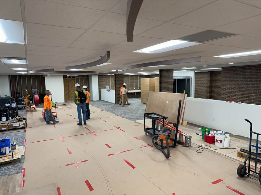 Image of the library first floor with ceiling in place and ceiling baffles being installed, several carpenters and other staff at work