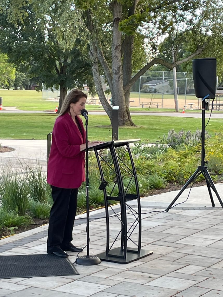 A woman speaking into a mic to a crowd of people in a sculpture park