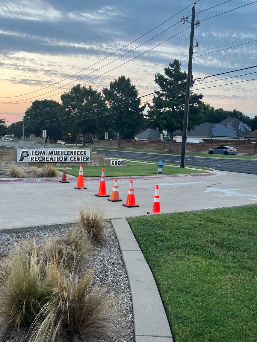 driveway entrance with orange and white construction cones surrounded by grass and landscaping 