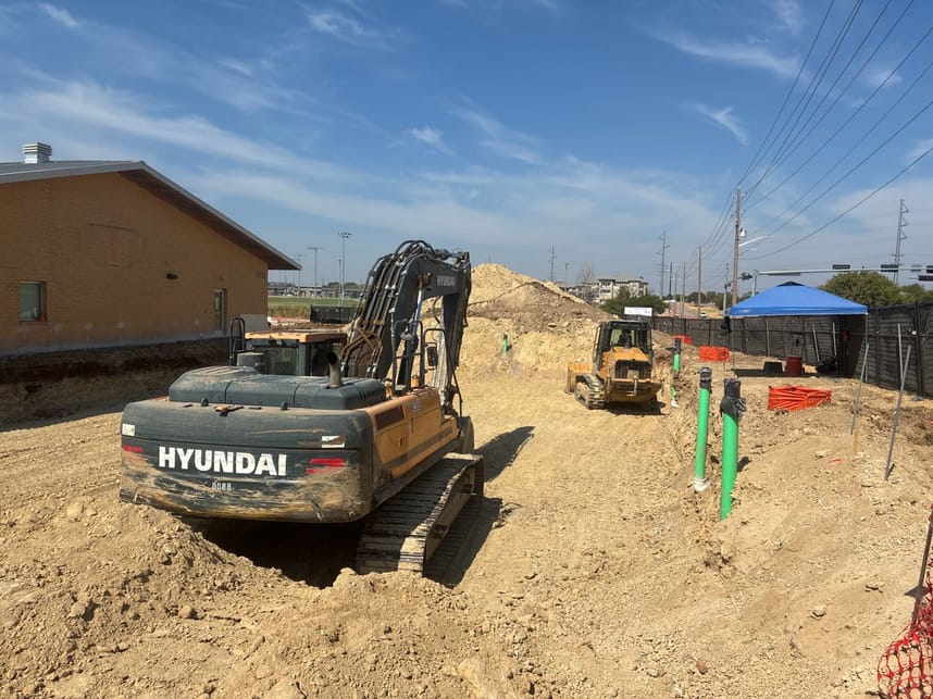 Large construction equipment in dirt, with plumbing pipes protruding from ground.