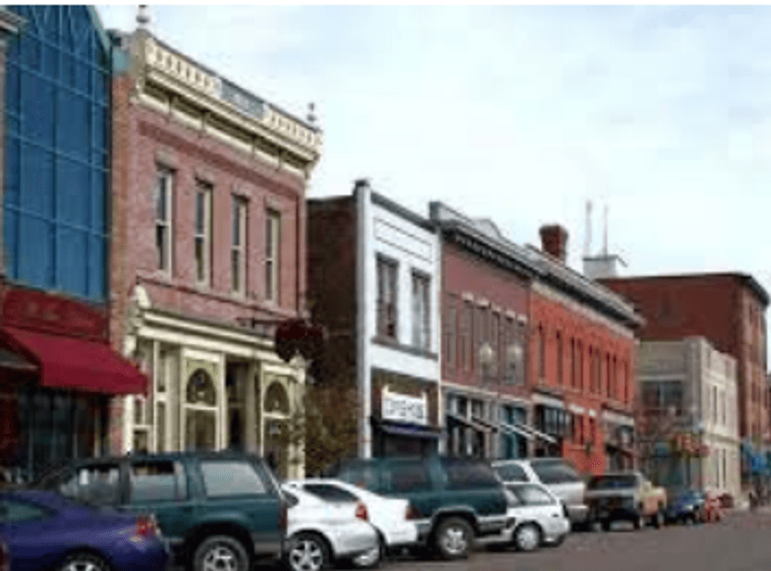 Historic downtown Laramie streetscape with multi-story commercial buildings, storefronts, and parked vehicles along the street.