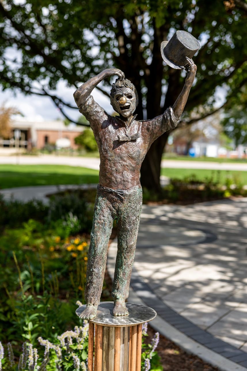 a 6' tall bronze, stainless steel and copper sculpture of a young man taking off a mask 