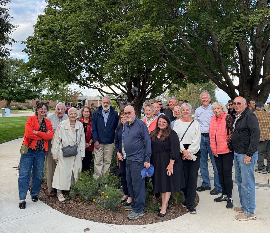 A group of smiling people surrounding a statue. 