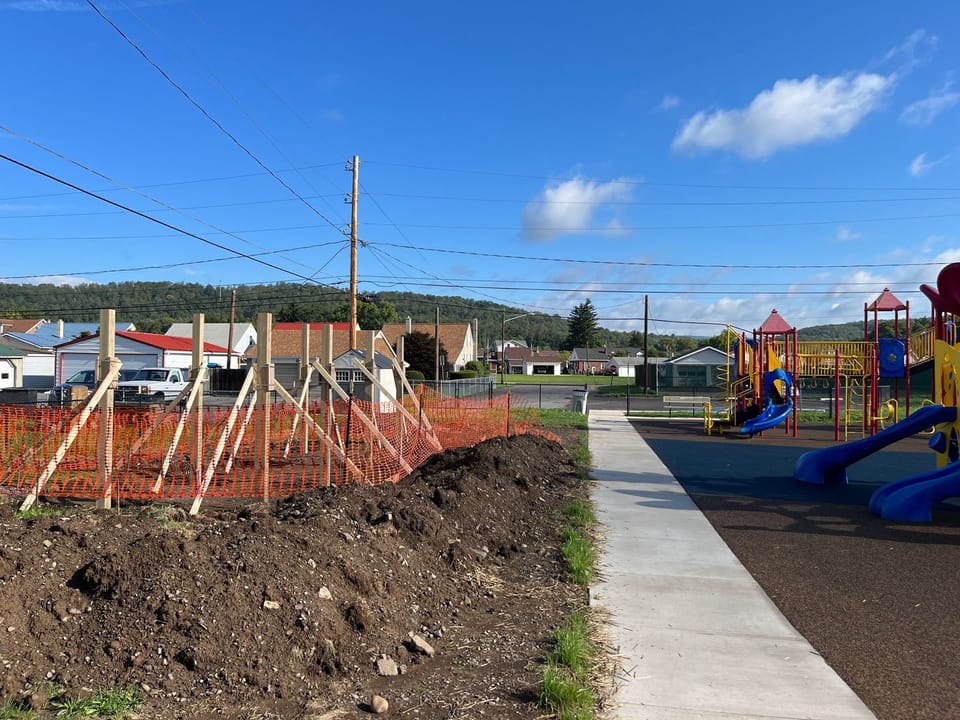 Image showing the construction of the pavilion at Piper Harmon Playground. Loose dirt can be seen with orange safety fencing to the left of the scene with posts for the pavilion set upright. The finish play area can be seen on the right side of the image.