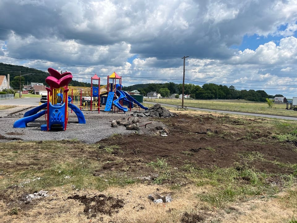 Photo showing the construction progress at Piper-Harmon Playground. The play structures still stand in the background will excavated dirt and chucks of broken asphalt are shown in the foreground.