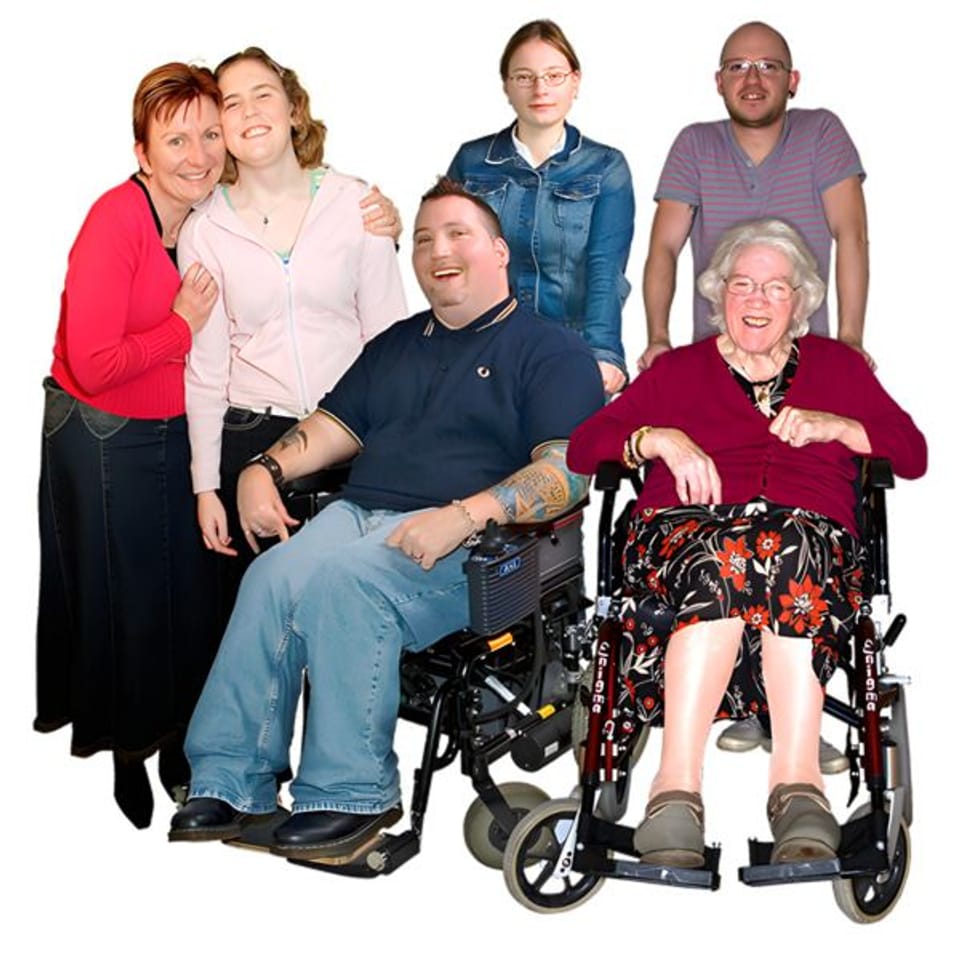 A diverse group of six people, including two in wheelchairs, smiling at the camera.